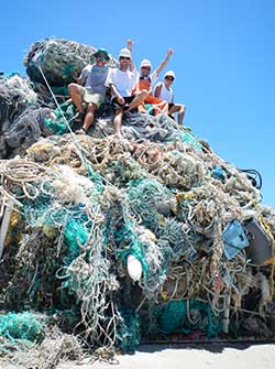 Participants of marine debris removal activities sit atop a mound of derelict fishing gear collected in Papahānaumokuākea Marine National Monument.