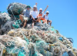Participants of marine debris removal activities sit atop a mound of derelict fishing gear collected in Papahānaumokuākea Marine National Monument.
