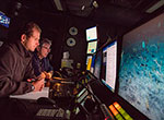 Expedition science leads Christopher Kelley (background) and Daniel Wagner (foreground) monitor an ROV dive in the science control room of the <em>Okeanos Explorer</em>.