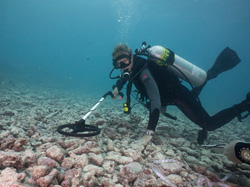 Cathy Green utilizes an underwater metal detector to locate artifacts not easily seen by the eye.