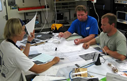 Cathy Green, Tane Casserley and Jason Raupp work on a site plan in the <em>Hiʻialakai</em>’s drylab.