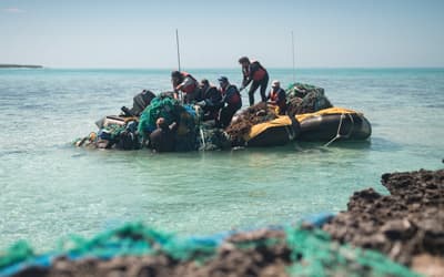 The marine debris team prepares to bring a huge conglomerate net onto a small boat. 