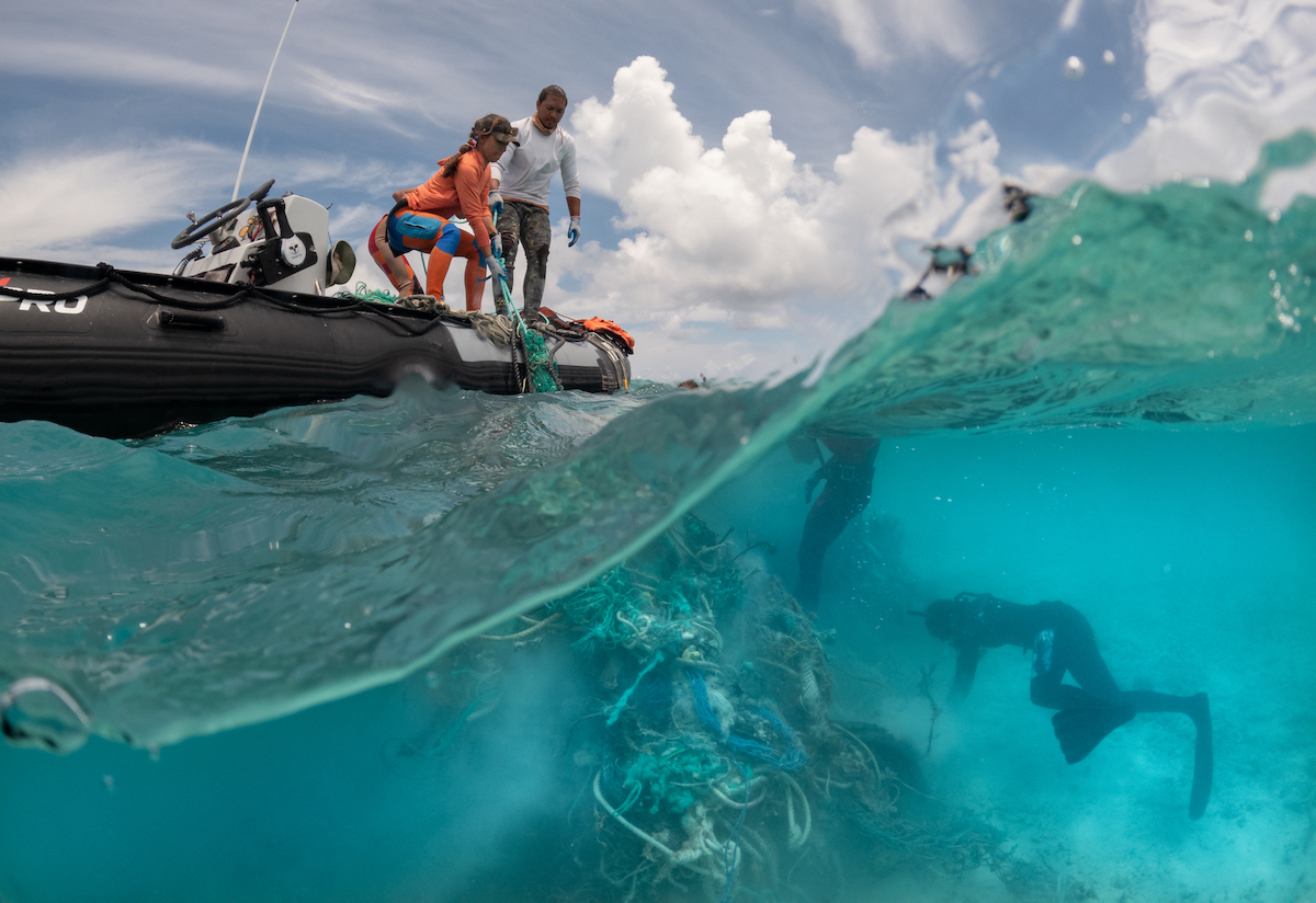 Small boat operators and freedivers pull up ghost nets from water.